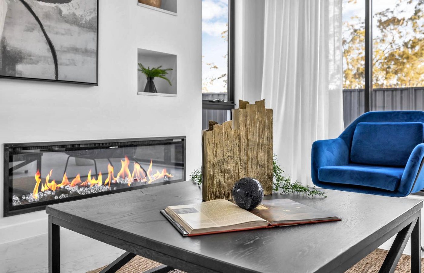 A study with a linear fireplace set into the wall, a dark desk and a blue velvet armchair